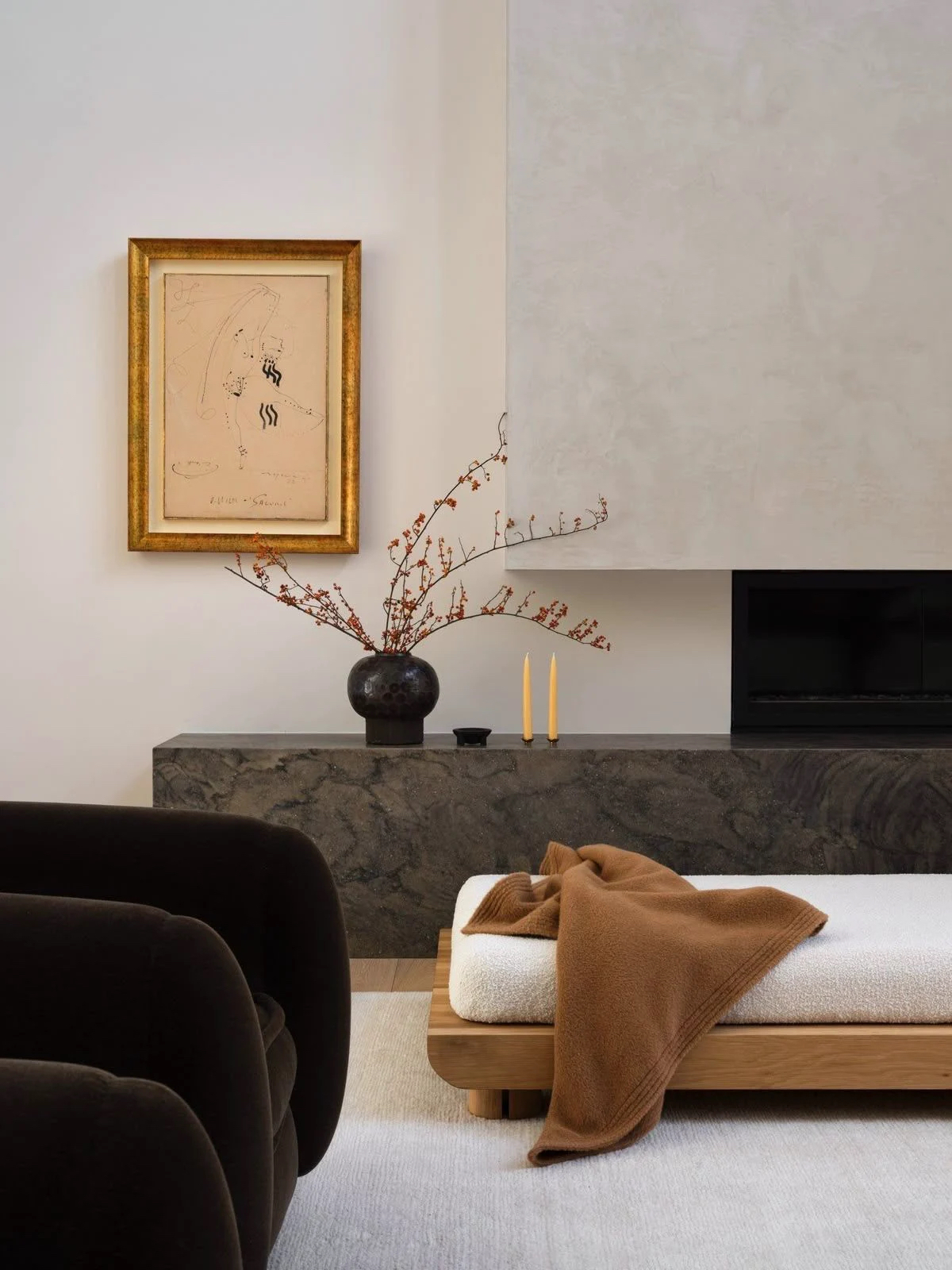 A calm living room with a dark velvet sofa, a stone fireplace ledge, and a bench with a camel throw